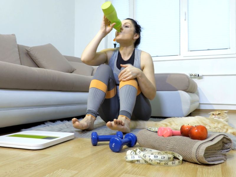 devojka sedi na podu i pije vodu nakon završenog kučnog treninga