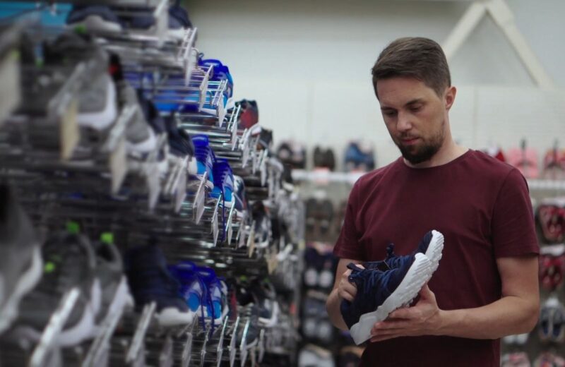 Muškarac u prodavnici obuće pažljivo pregleda patiku sa belim đonom